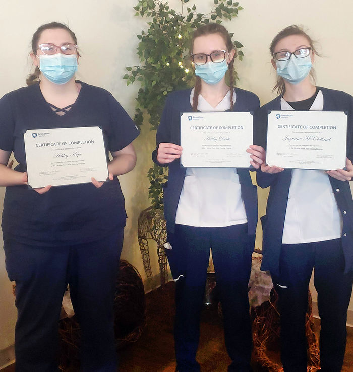 Three female students wearing masks and holding up certificates.