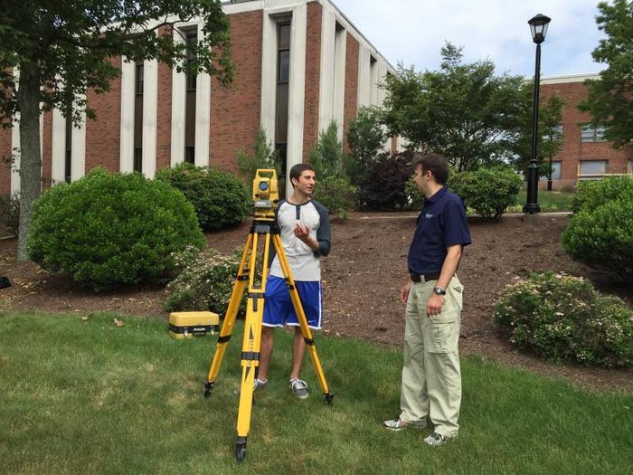A student looks through surveying equipment as an instructor looks on.