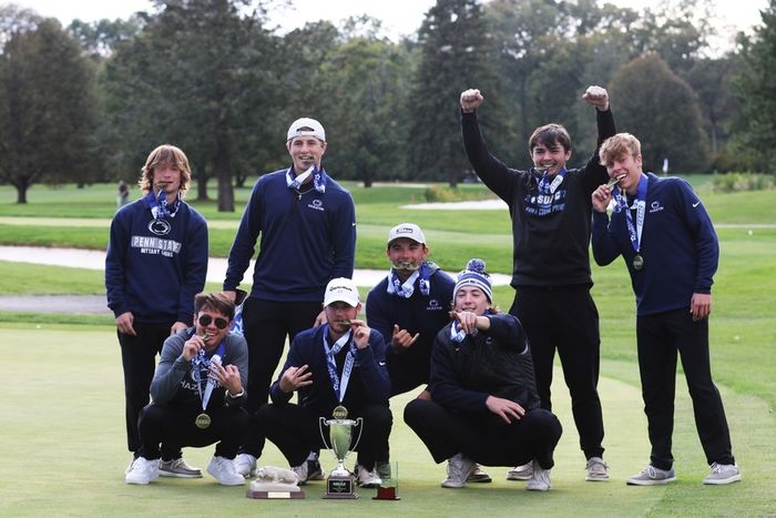 Group of eight students on a golf course holding golden medals and celebrating.