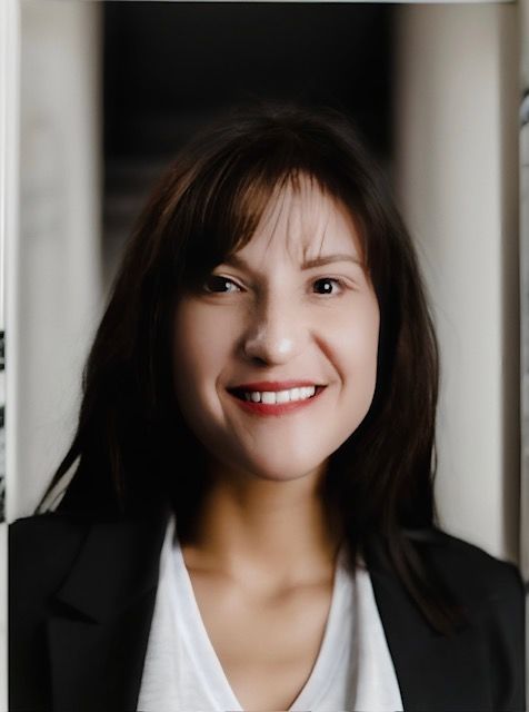 Woman with dark hair smiling in front of white/black background.