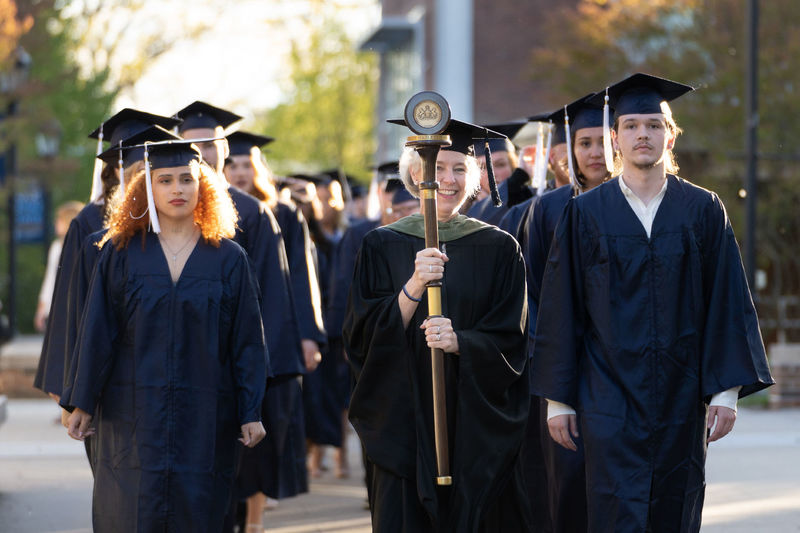 Two rows of students in caps and gowns processing down a sidewalk.