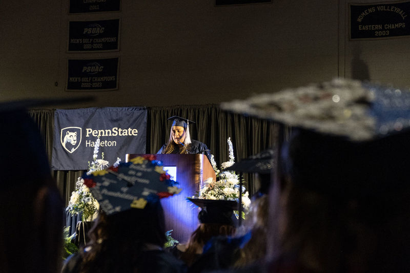 A woman in a cap and gown speaking from a podium on a stage.