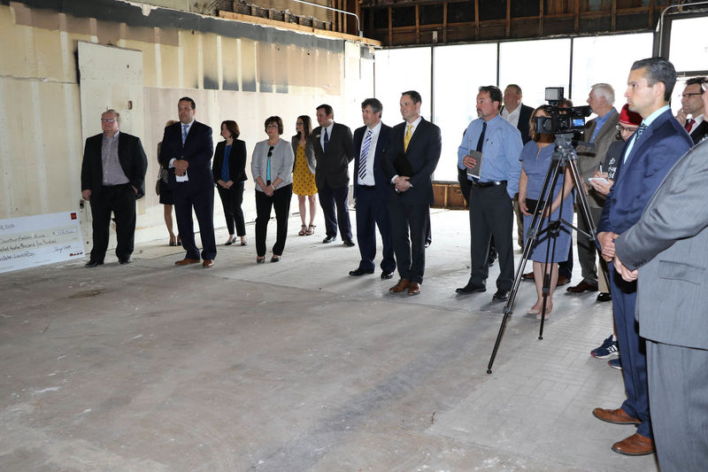 Group of people standing in a building undergoing renovation and watching a check presentation. 