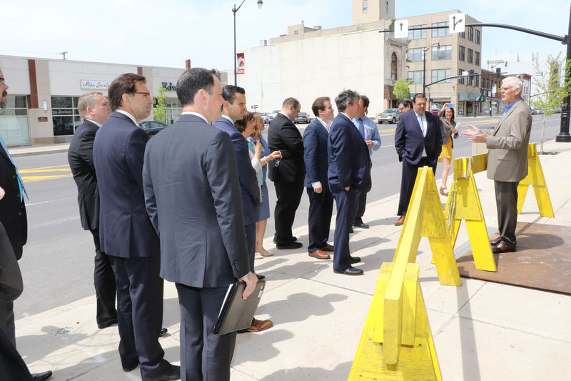 Man standing behind yellow construction barrier talking to a group of business people. 