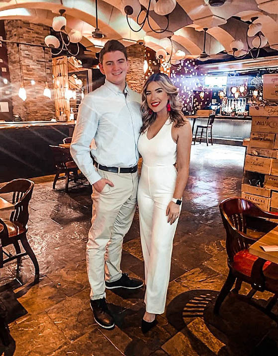 Man in white dress shirt and dress pants standing next to woman inside restaurant.