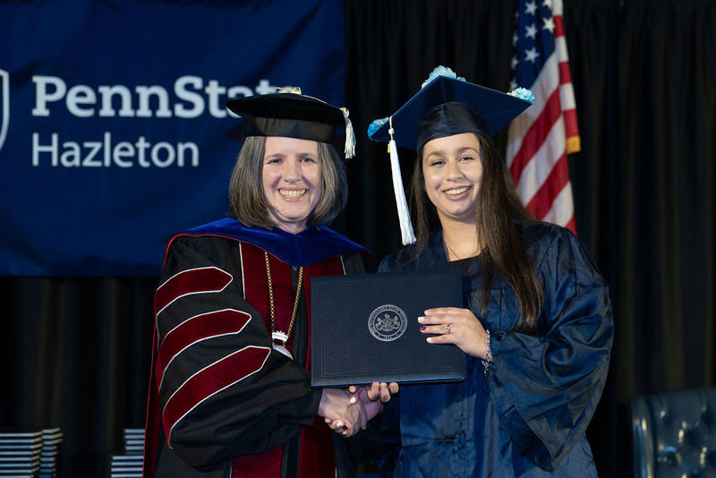 Graduate holding her diploma cover and shaking the hand of the chancellor.