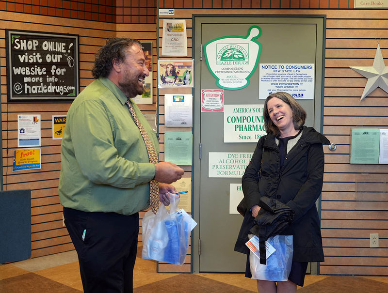 Man and woman laughing during conversation inside a pharmacy waiting area.