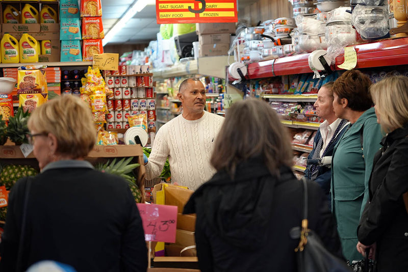 Grocery store owner speaking to group of people gathered inside store.