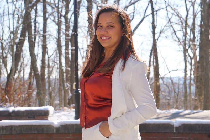 Woman dressed in business casual, white pantsuit, outdoors with snow and trees in background. 