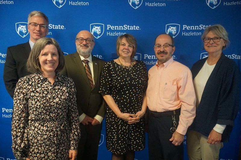Six men and women smiling in front of a Penn State Hazleton backdrop.