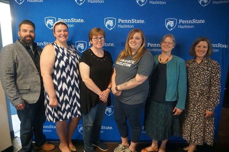 Group of five people posing in front of Penn State background.