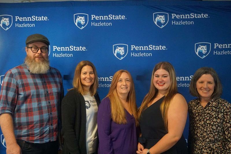 Group of five people posing in front of Penn State background.