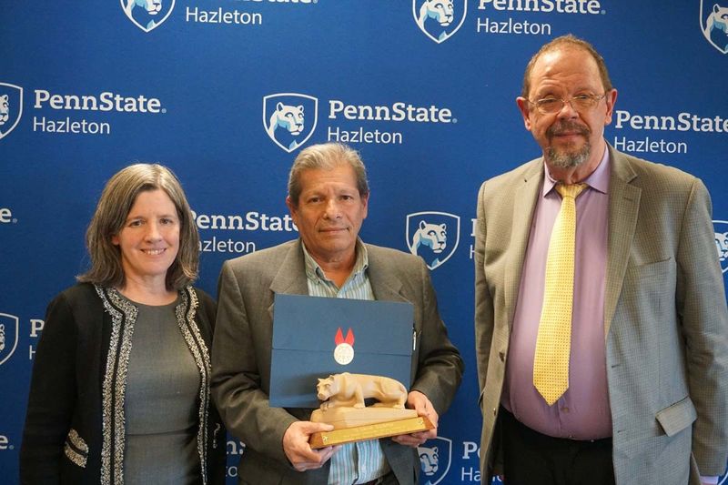 Man standing with miniature Nittany Lion statue and certificate with man and women at his side.