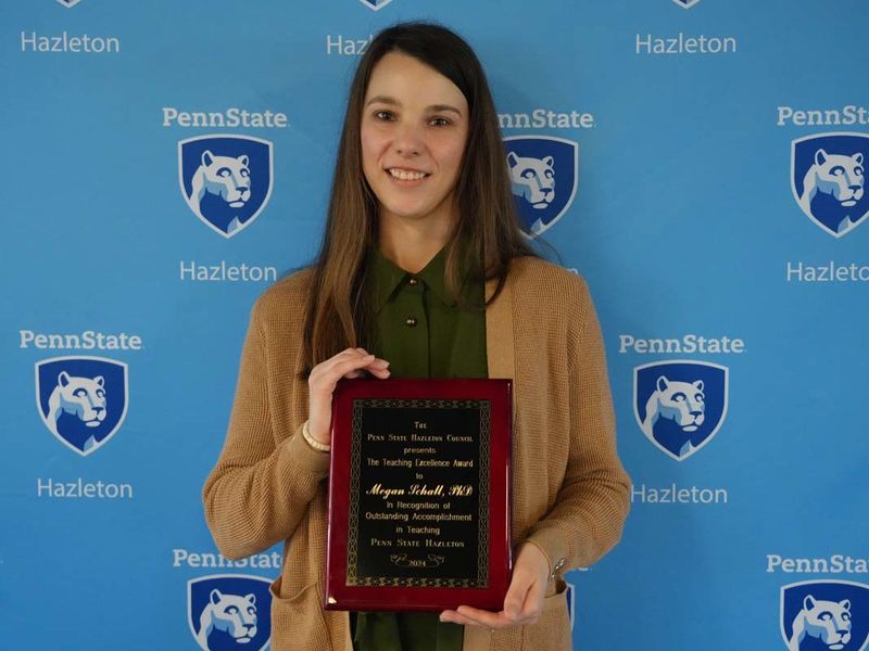 Woman holding plaque in front of light blue Penn State Hazleton backdrop.