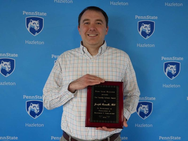 Man holding plaque in front of light blue Penn State Hazleton backdrop.