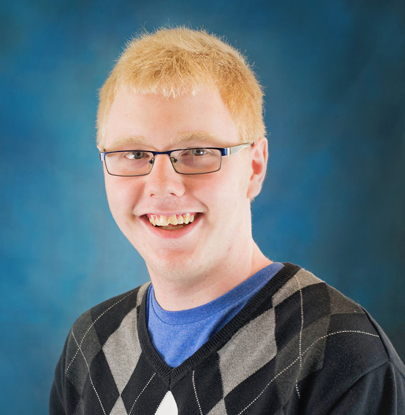 Man in plaid sweater with blue undershirt and glasses.