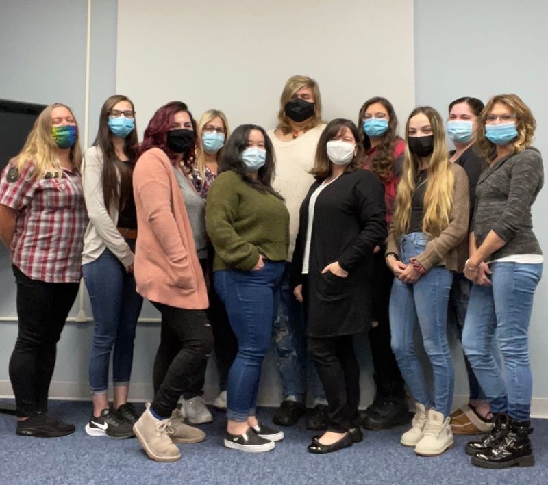 Group of women wearing masks and standing in a row inside a classroom.