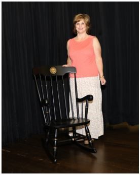 Woman standing next to rocking chair.
