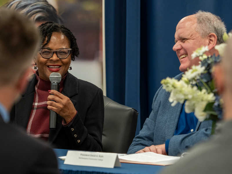 a woman smiles next to a man as she speaks into a microphone