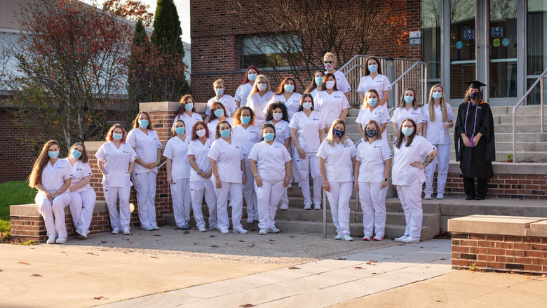 Rows of practical nursing students in white scrubs lined up on steps in front of campus building.