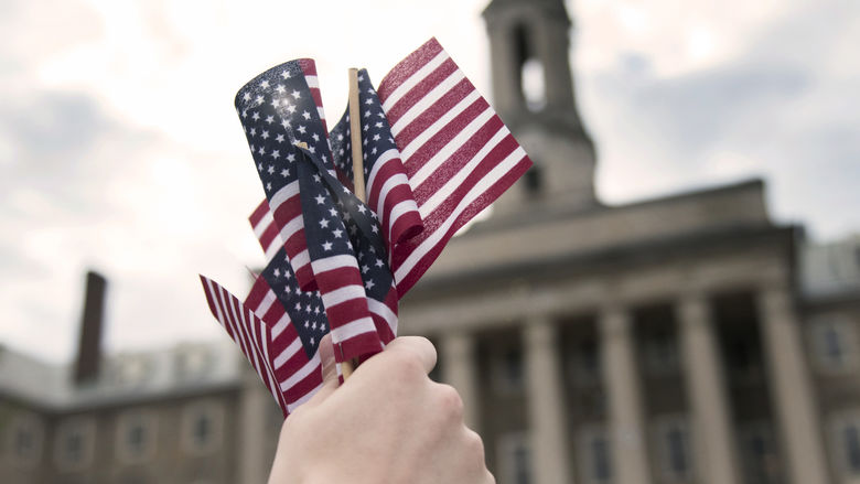 A person holds a group of mini American flags in front of the Old Main building on Penn State's University Park campus.