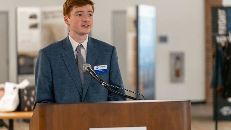 Male student in suit speaking from a podium.