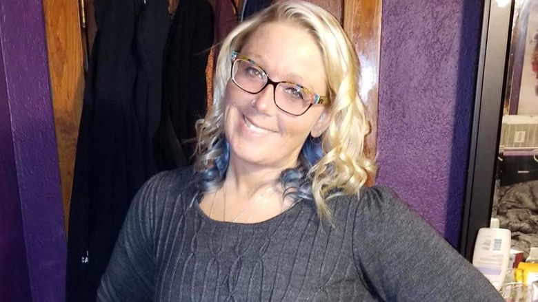 Woman with blonde hair and glasses in a gray dress.