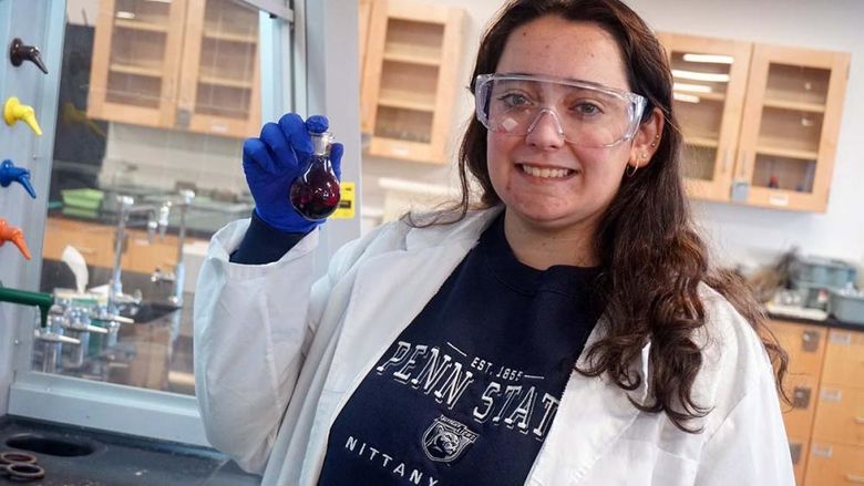 Woman in lab coat holding beaker of purple liquid in a science laboratory.