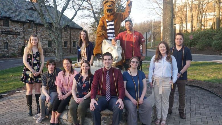 Group of students seated surrounding statue of Nittany Lion in grass field.