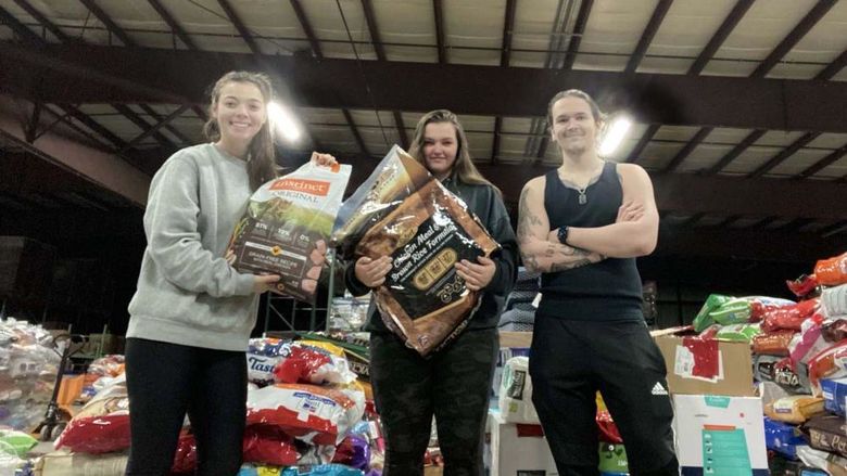 Three students standing in front of stacks of pet food in a warehouse.