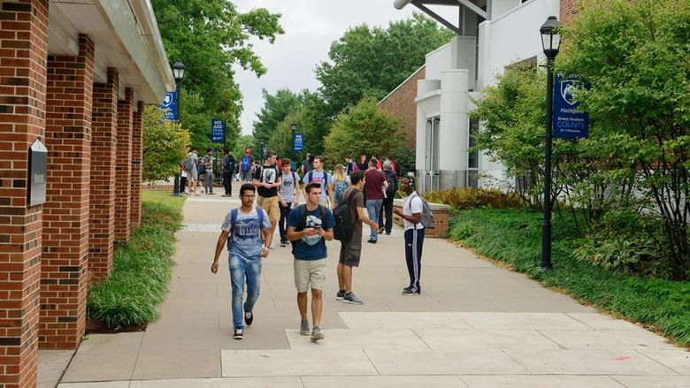 Crowd of students walking along a sidewalk on a college campus.
