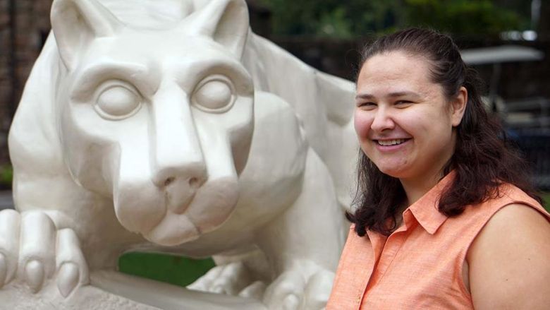 Woman with brown hair and salmon-colored blouse smiling next to stone statue of a lion.