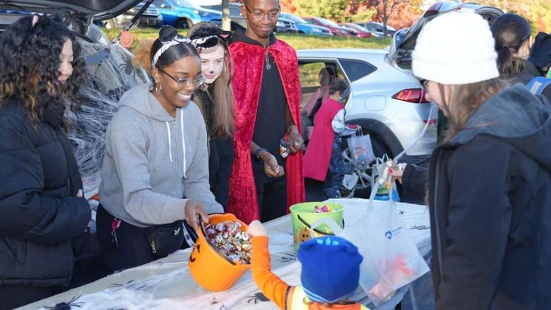 Students in Halloween costumes handing out candy to child in a costume.