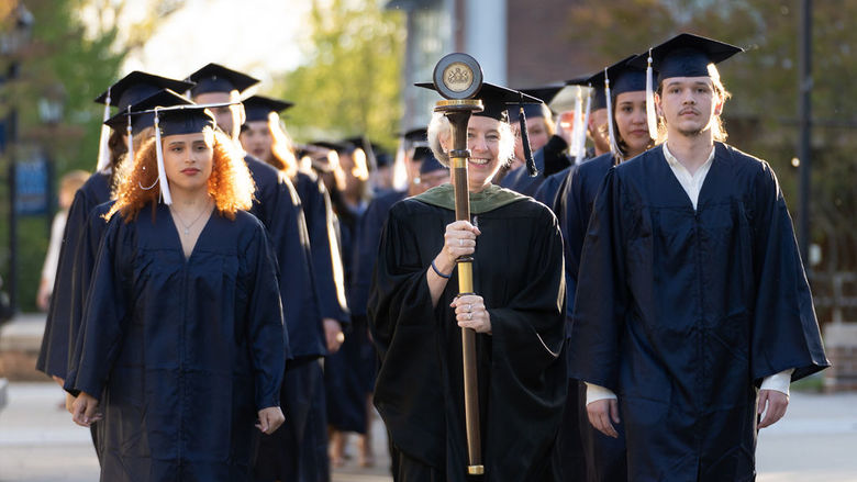 Two rows of graduates in caps and gowns walking towards camera