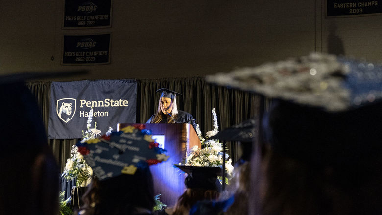 A woman in a cap and gown speaking from a podium on a stage.