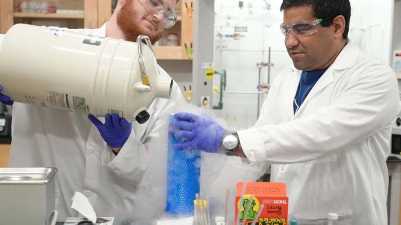 A student and professor in white lab coats pouring liquid nitrogen in a lab