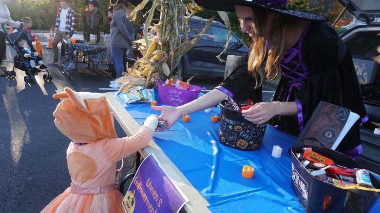 A Penn State Hazleton student dressed in a witch's costume hands candy to a young child dressed as Bingo from Bluey. 