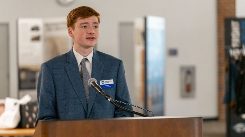 Male student in a light blue suit speaking from a podium.