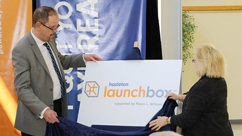 Penn State Hazleton Chancellor Gary Lawler, left, and Linda Schiavo unveil the logo for the Hazleton LaunchBox, which will be named after Linda's brother, the late Pasco L. Schiavo.