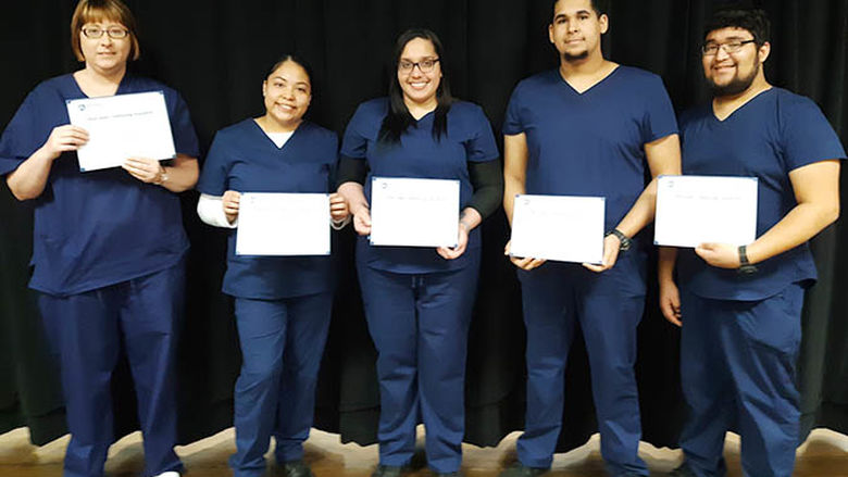 Five students in scrubs holding certificates 