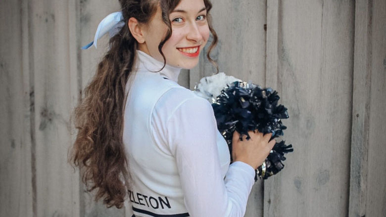 Cheerleader smiling and holding pom-pom.