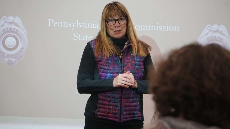 Woman with glasses and long blonde hair standing in front of projector screen in classroom.