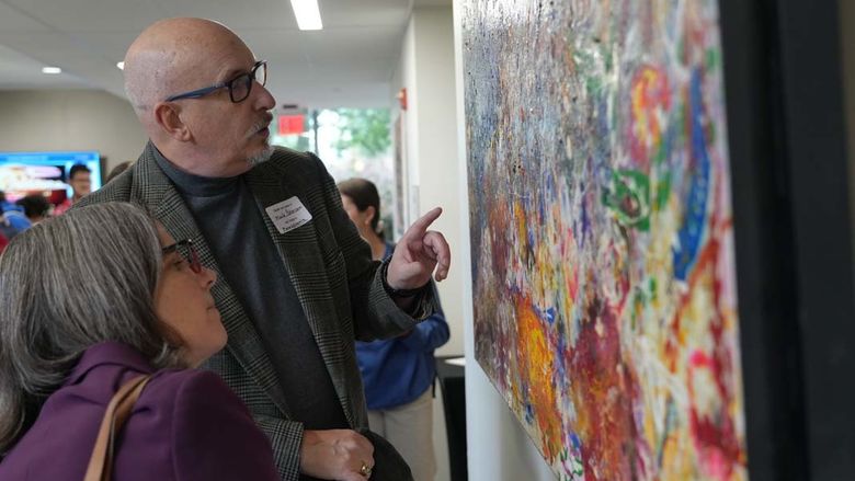 Man and woman looking closely at a colorful painting hanging on a wall.