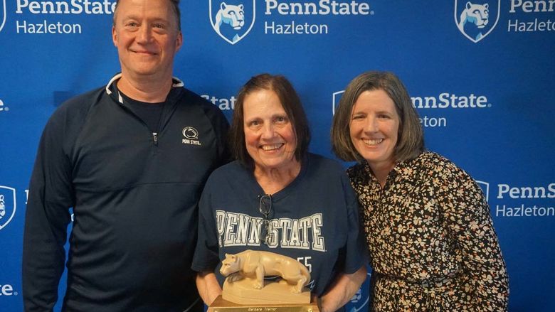 Woman holding miniature Nittany Lion statue standing next to another man and woman.