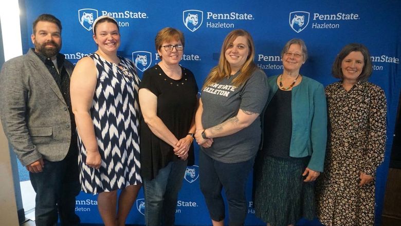 Group of five people posing in front of Penn State background.