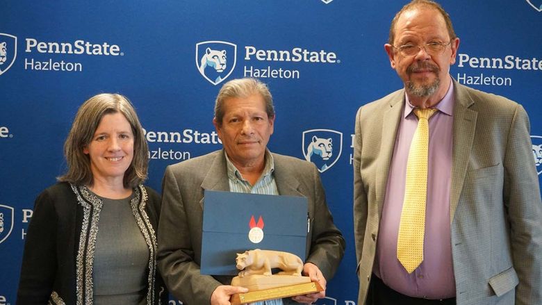 Man standing with miniature Nittany Lion statue and certificate with man and women at his side.