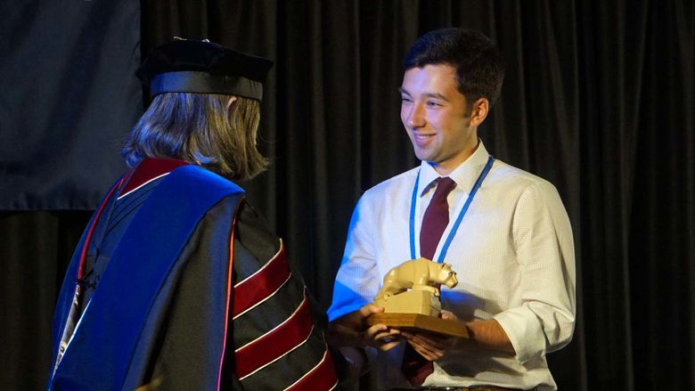Student in white dress shirt and tie being handed a miniature statue of Nittany Lion.