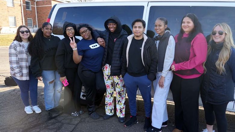 A group of students in a row lined up outside a white van in a parking lot.