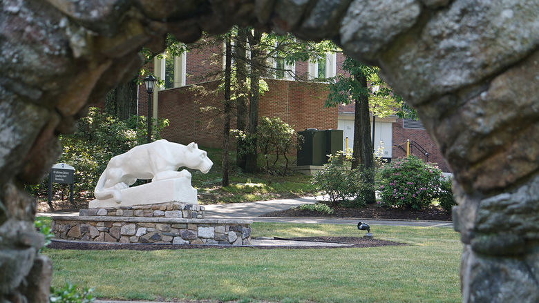 A stone lion statue in a grassy area with a stone archway in the foreground
