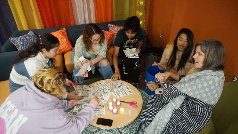Students sitting in a circle around a table doing arts and crafts.